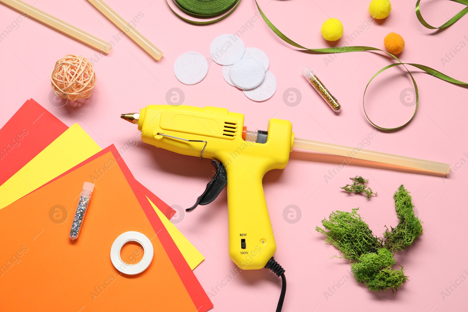 Photo of Hot glue gun and handicraft materials on pink background, flat lay