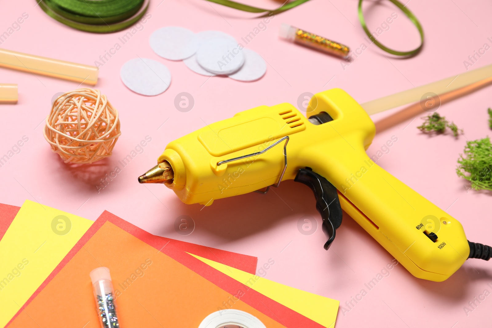 Photo of Hot glue gun and handicraft materials on pink background, closeup