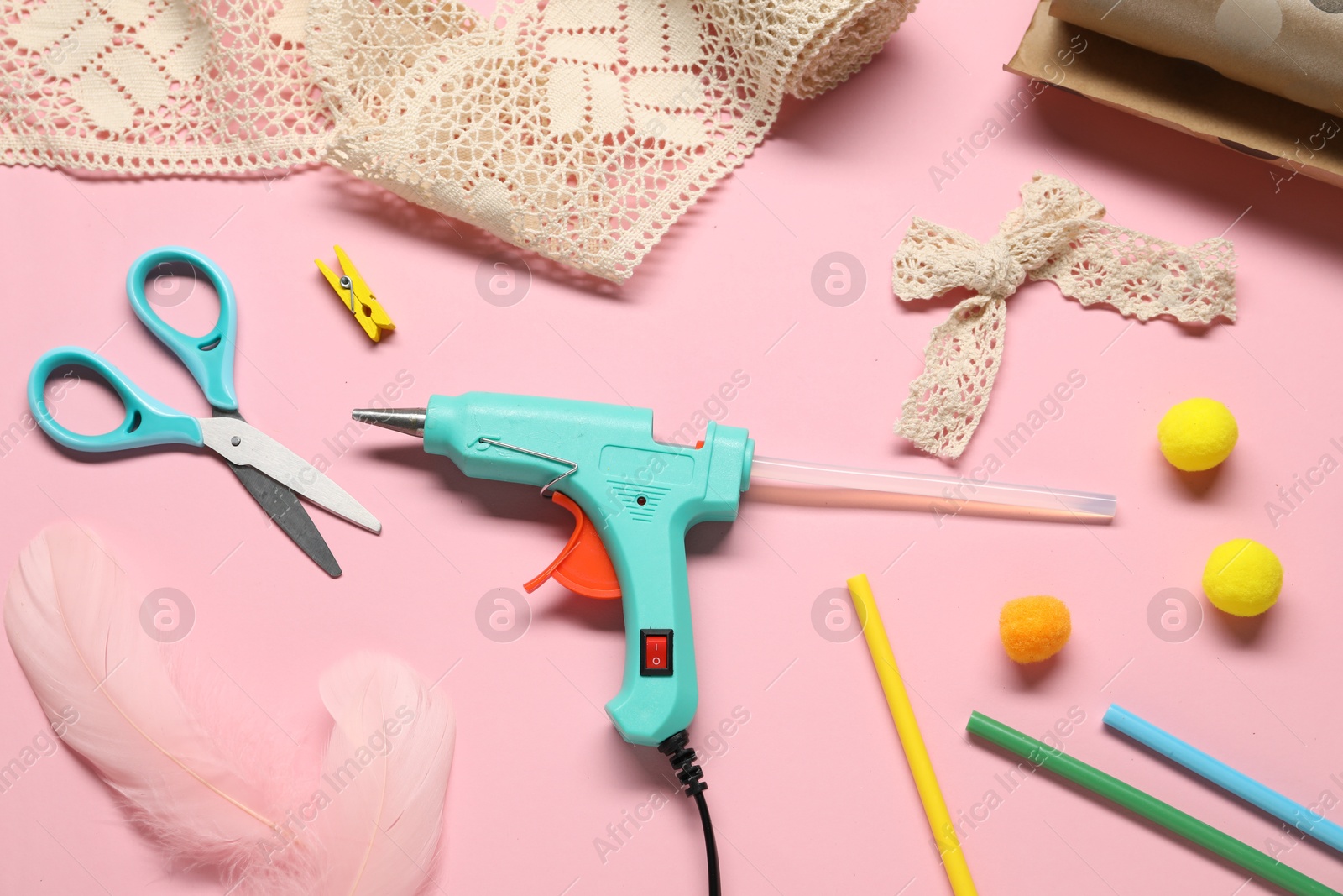 Photo of Hot glue gun and handicraft materials on pink background, flat lay