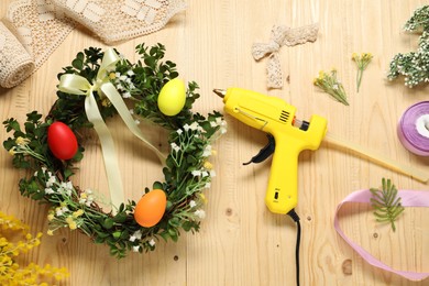 Photo of Hot glue gun and handicraft materials on wooden background, flat lay