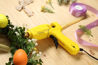 Photo of Hot glue gun and handicraft materials on wooden background, closeup