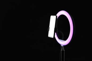 Photo of Ring lamp with smartphone on black background, space for text