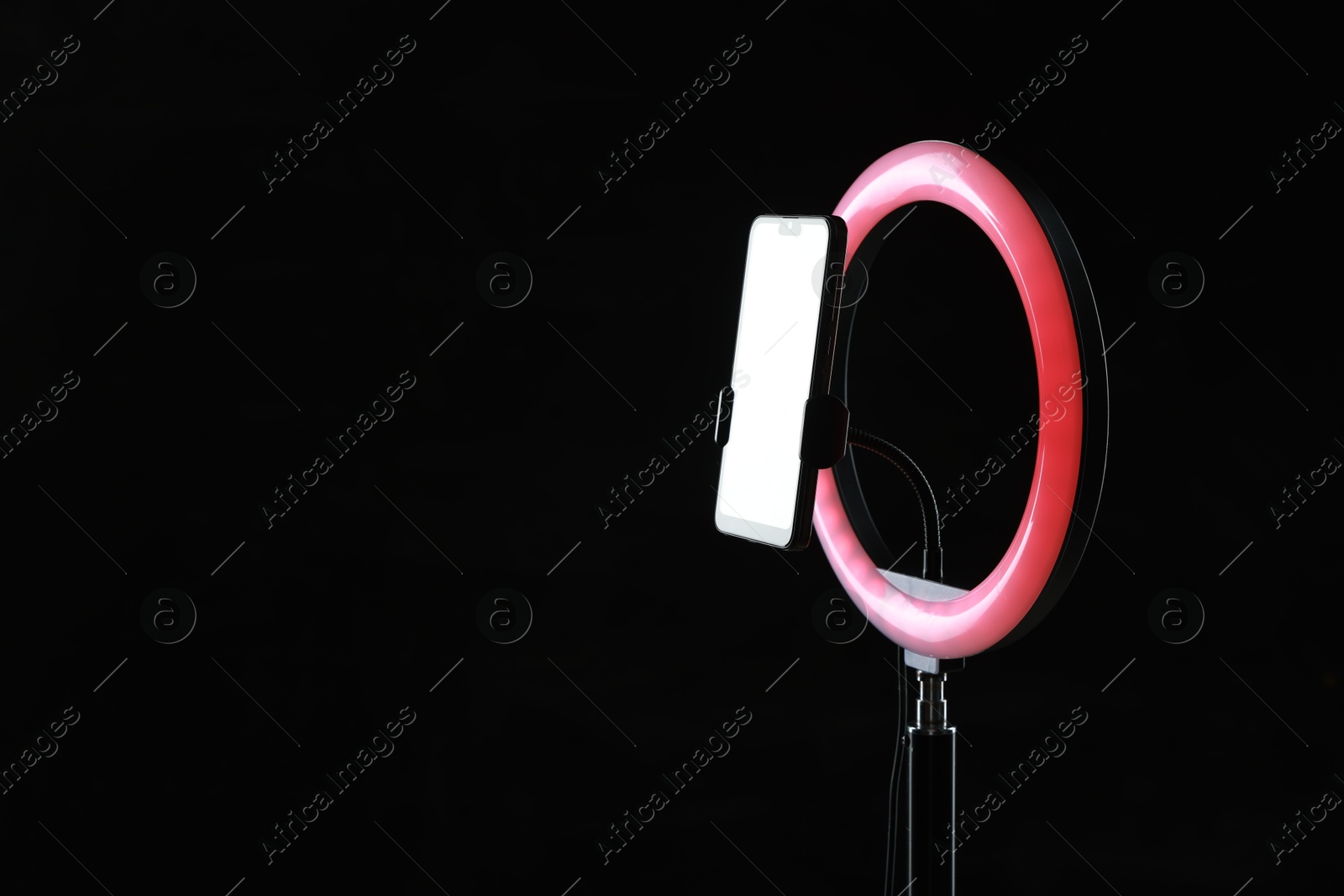 Photo of Ring lamp with smartphone on black background, space for text