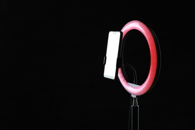 Photo of Ring lamp with smartphone on black background, space for text