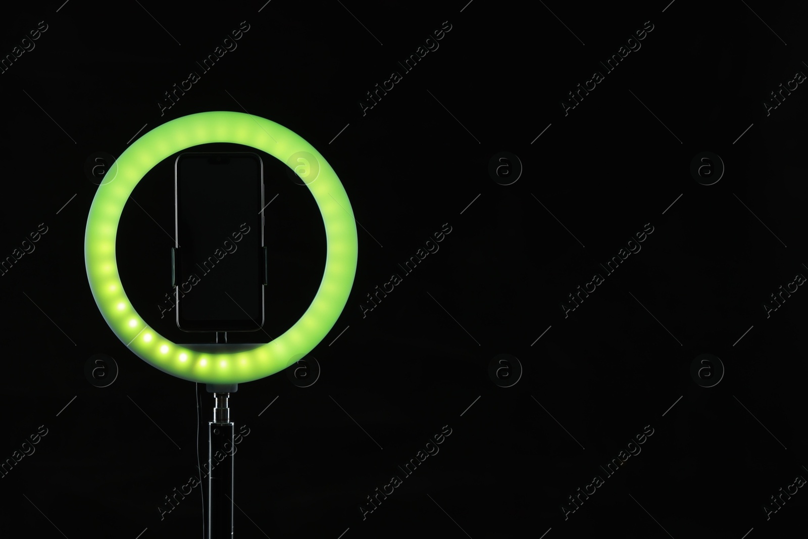 Photo of Ring lamp with smartphone on black background, space for text