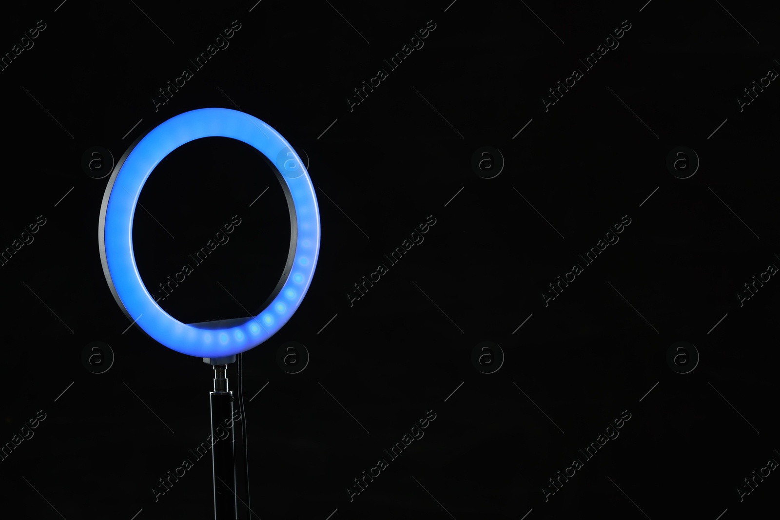 Photo of Ring lamp on stand against black background, space for text