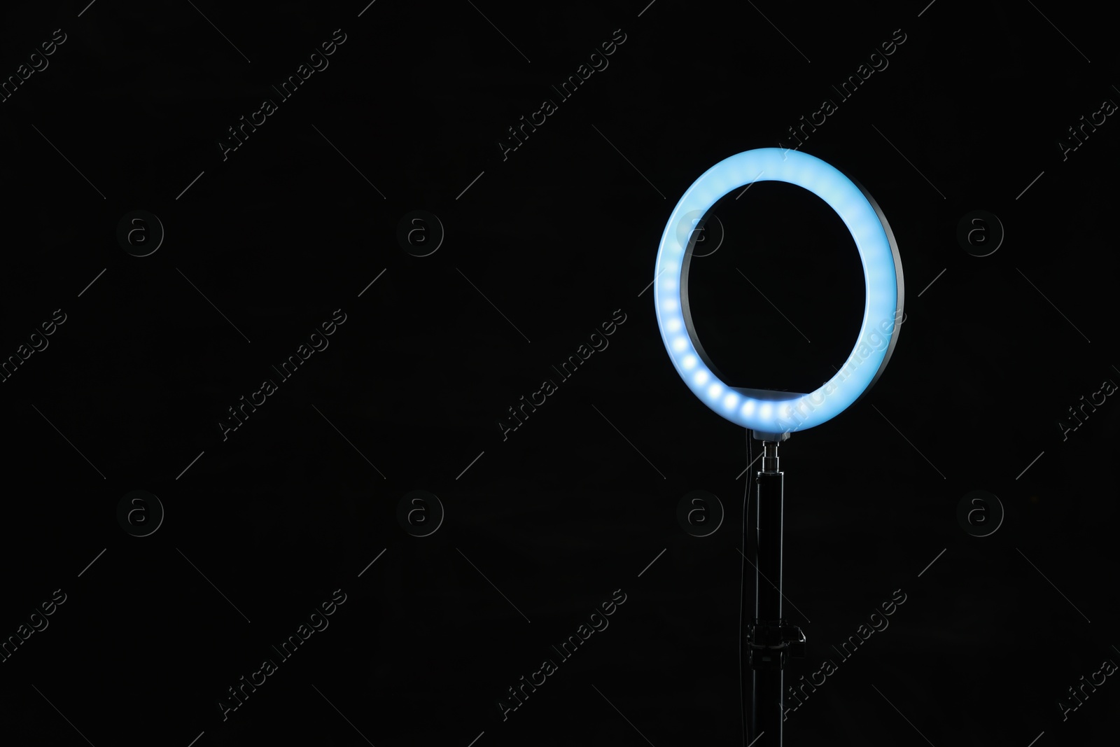 Photo of Ring lamp on stand against black background, space for text