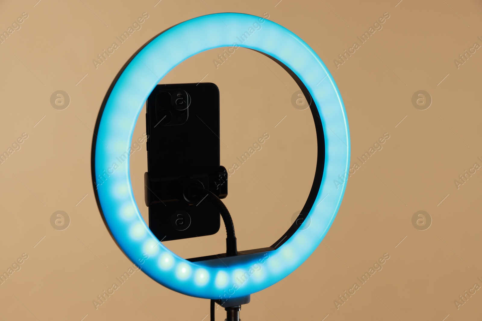 Photo of Ring lamp with smartphone on beige background, closeup