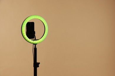 Photo of Ring lamp with smartphone on beige background, space for text