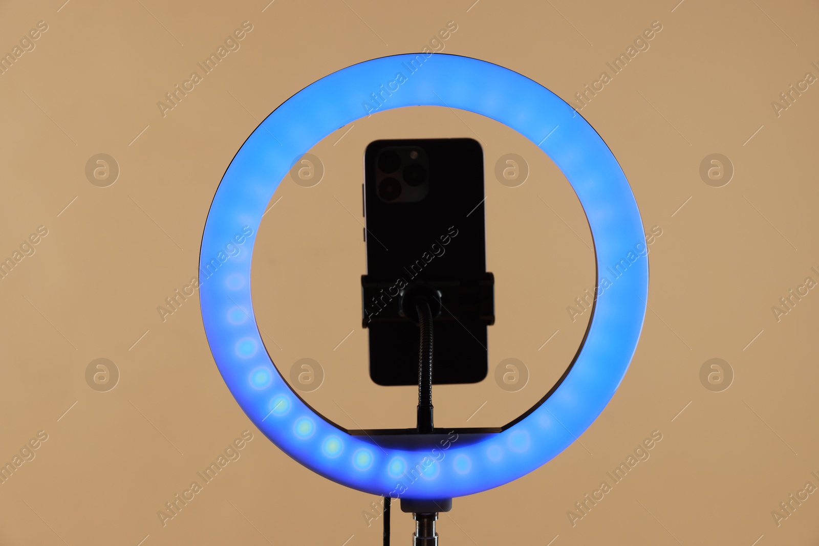 Photo of Ring lamp with smartphone on beige background