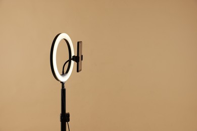 Photo of Ring lamp with smartphone on beige background, space for text