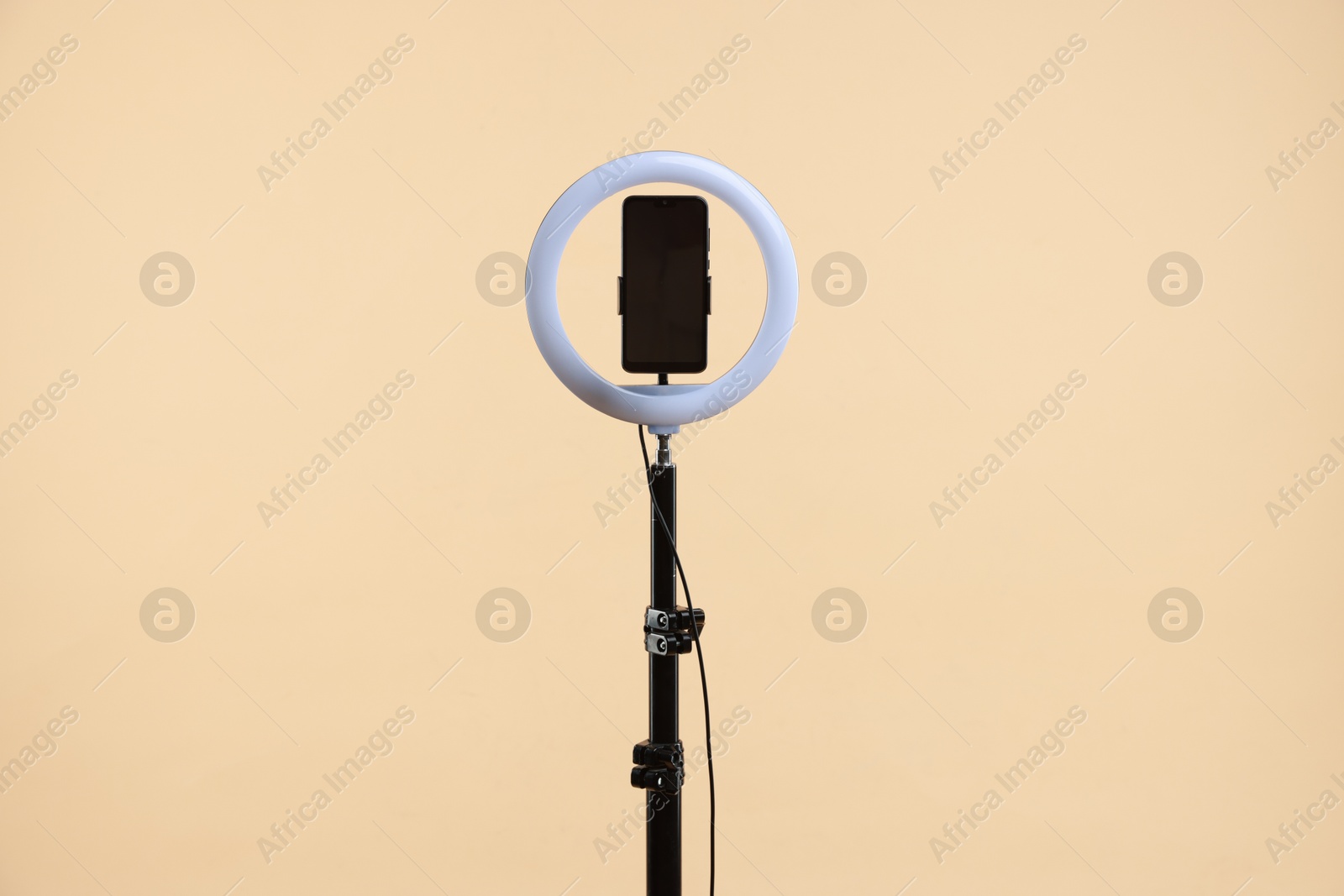 Photo of Ring lamp with smartphone on beige background