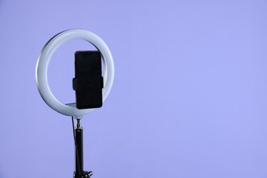 Photo of Ring lamp with smartphone on purple background, space for text