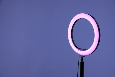 Photo of Ring lamp on stand against purple background, space for text