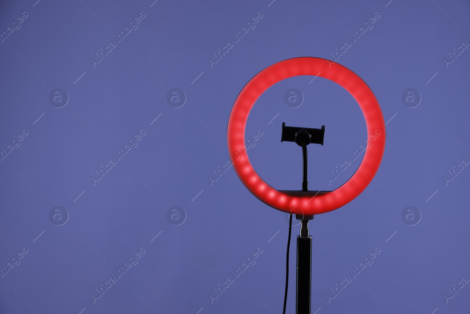 Photo of Ring lamp with holder for smartphone against purple background, space for text