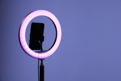 Photo of Ring lamp with smartphone on purple background, space for text