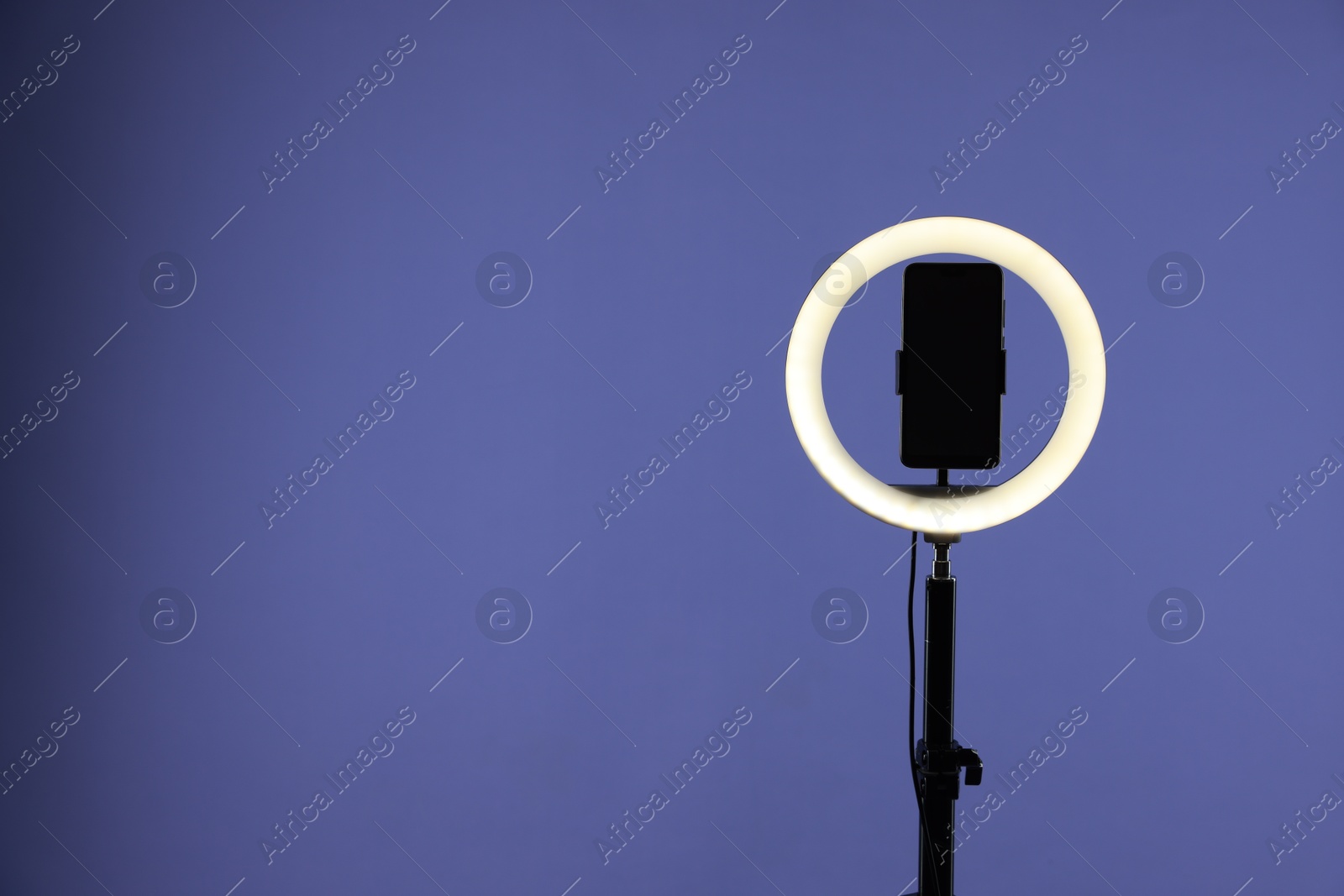 Photo of Ring lamp with smartphone on purple background, space for text