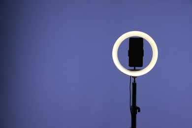 Photo of Ring lamp with smartphone on purple background, space for text