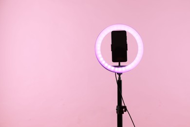 Photo of Ring lamp with smartphone on pink background, space for text