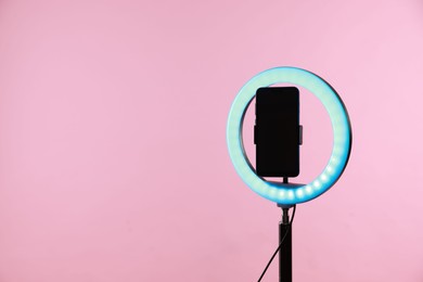 Photo of Ring lamp with smartphone on pink background, space for text