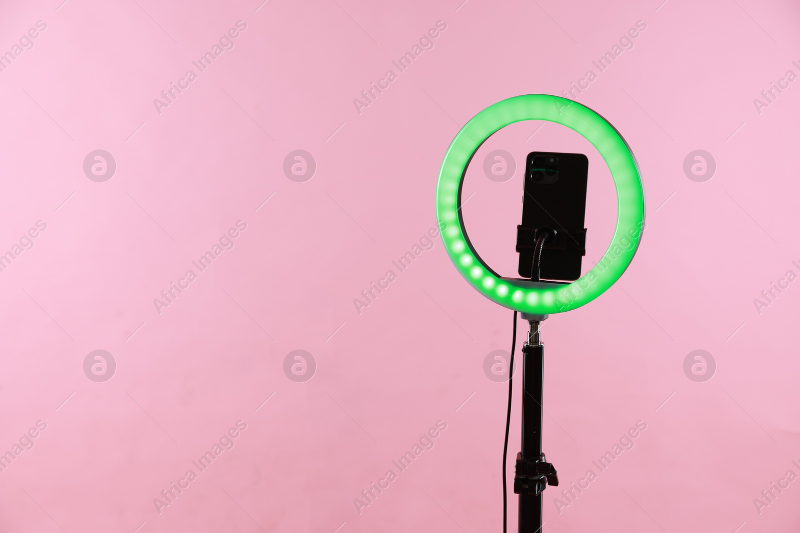 Photo of Ring lamp with smartphone on pink background, space for text