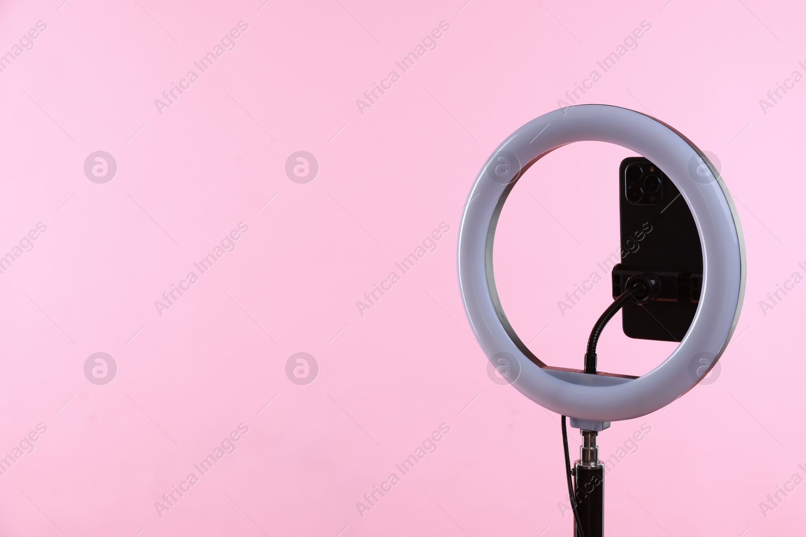 Photo of Ring lamp with smartphone on pink background, space for text