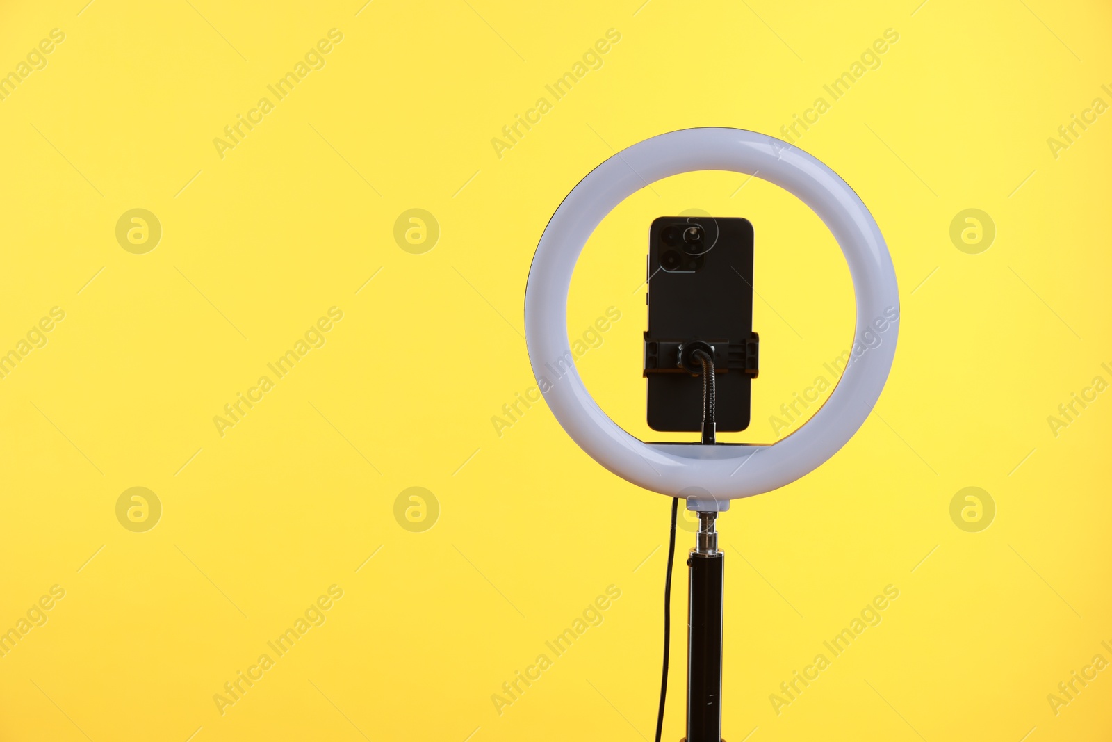 Photo of Ring lamp with smartphone on yellow background, space for text