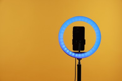 Photo of Ring lamp with smartphone on orange background, space for text