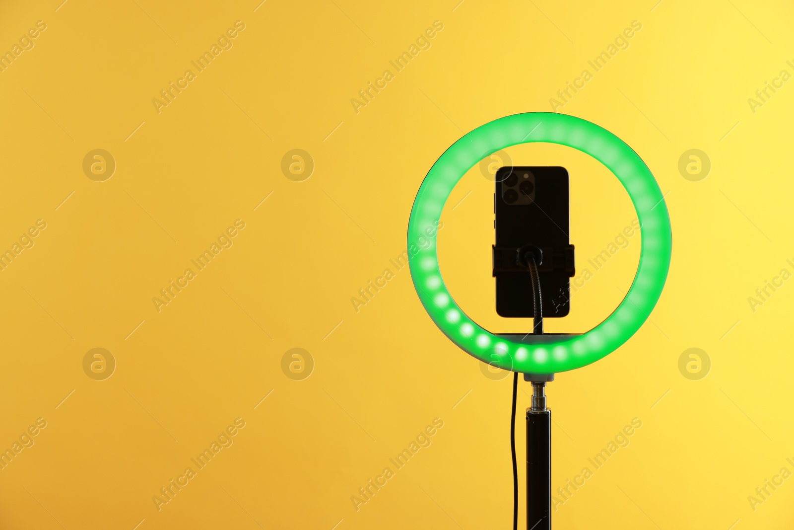 Photo of Ring lamp with smartphone on orange background, space for text