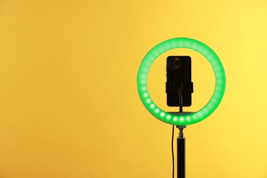 Photo of Ring lamp with smartphone on orange background, space for text