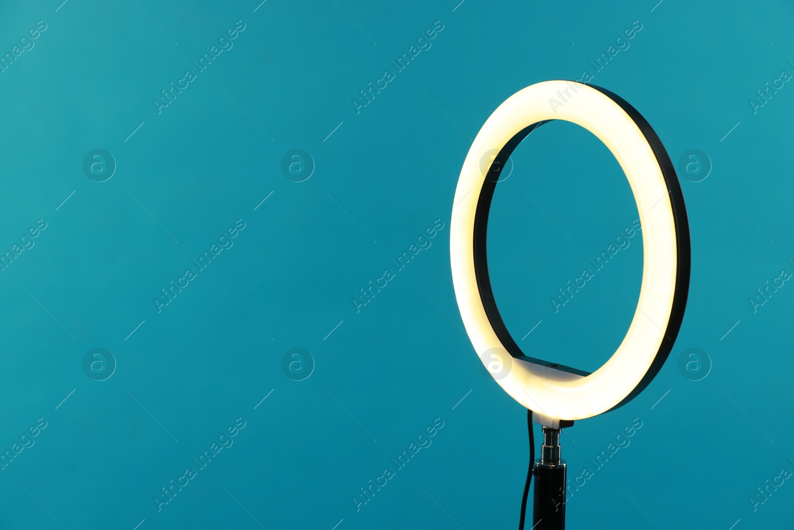 Photo of Ring lamp on stand against light blue background, space for text