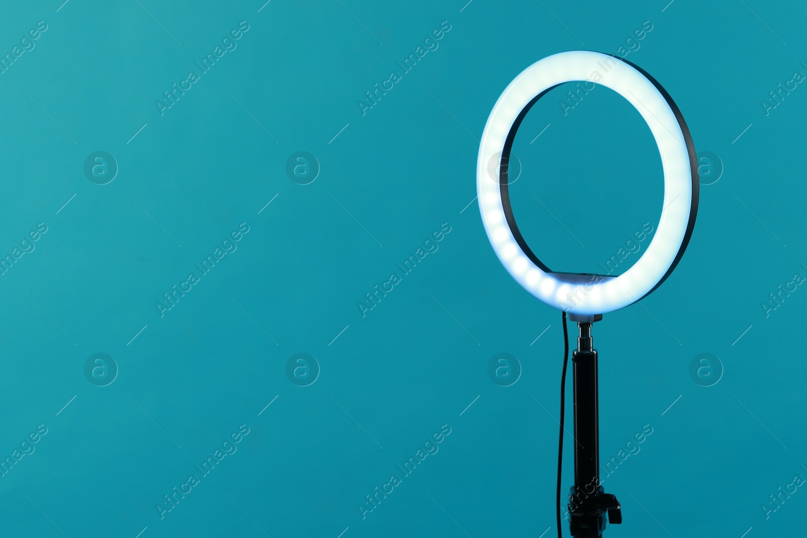 Photo of Ring lamp on stand against light blue background, space for text