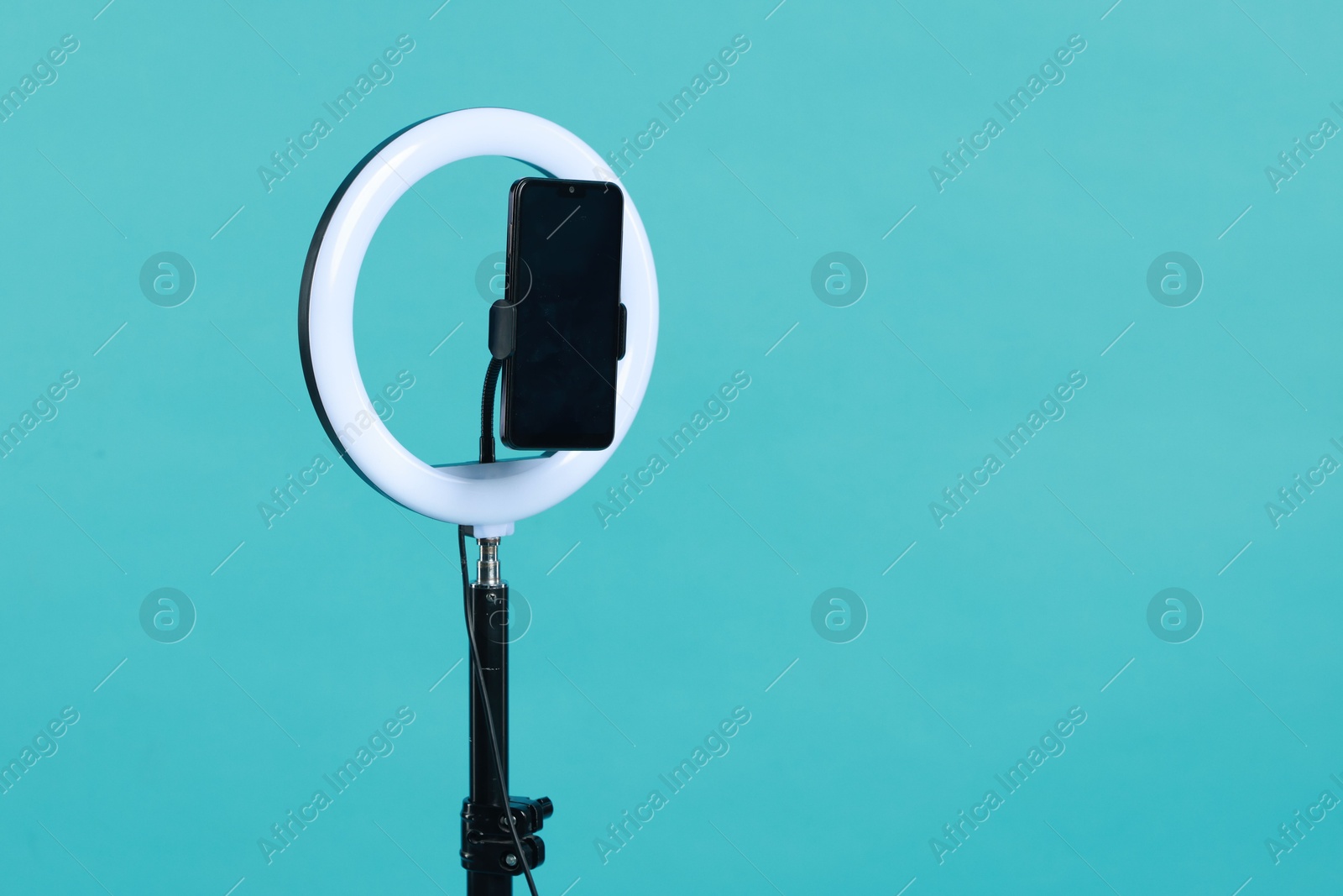 Photo of Ring lamp with smartphone on light blue background, space for text