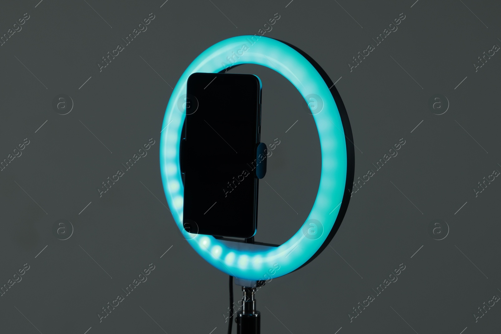 Photo of Ring lamp with smartphone on grey background, closeup