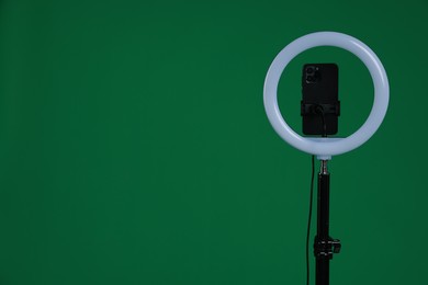 Photo of Ring lamp with smartphone on green background, space for text