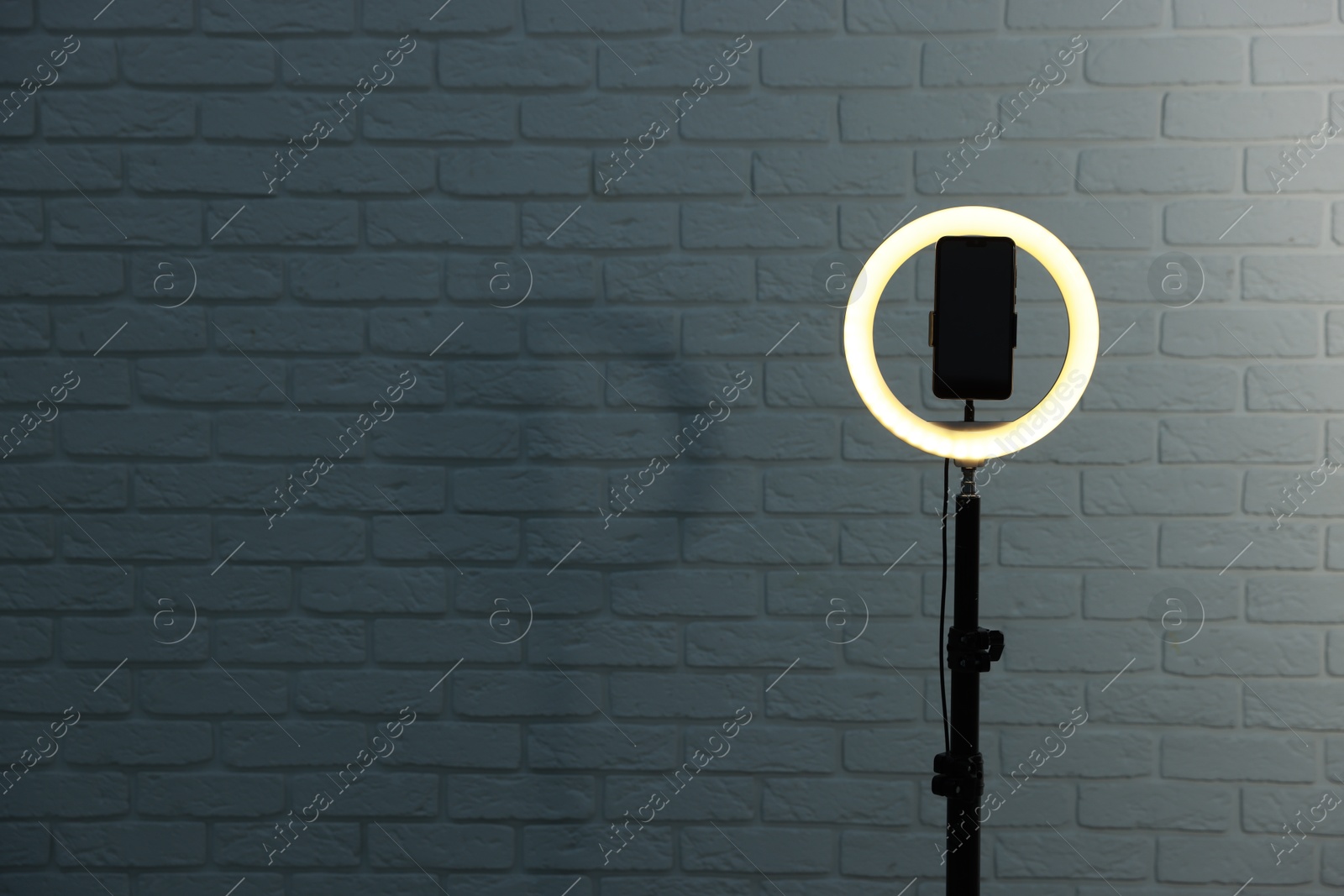 Photo of Ring lamp with smartphone against brick wall, space for text