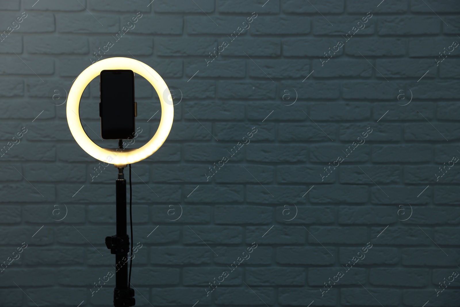 Photo of Ring lamp with smartphone against brick wall, space for text