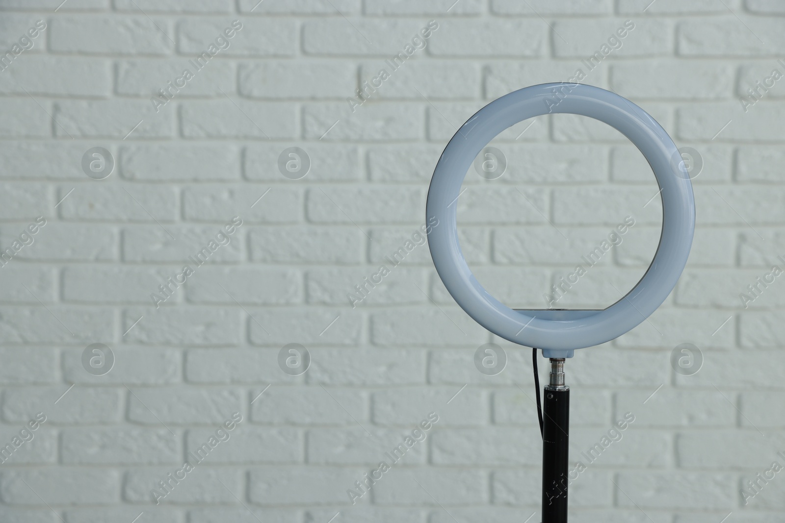 Photo of Ring lamp on stand against white brick wall, space for text