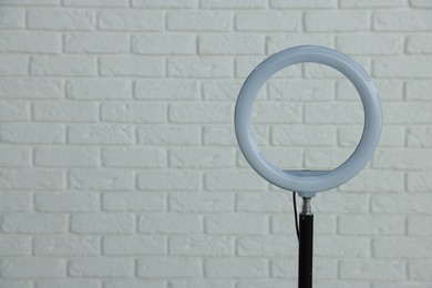 Photo of Ring lamp on stand against white brick wall, space for text