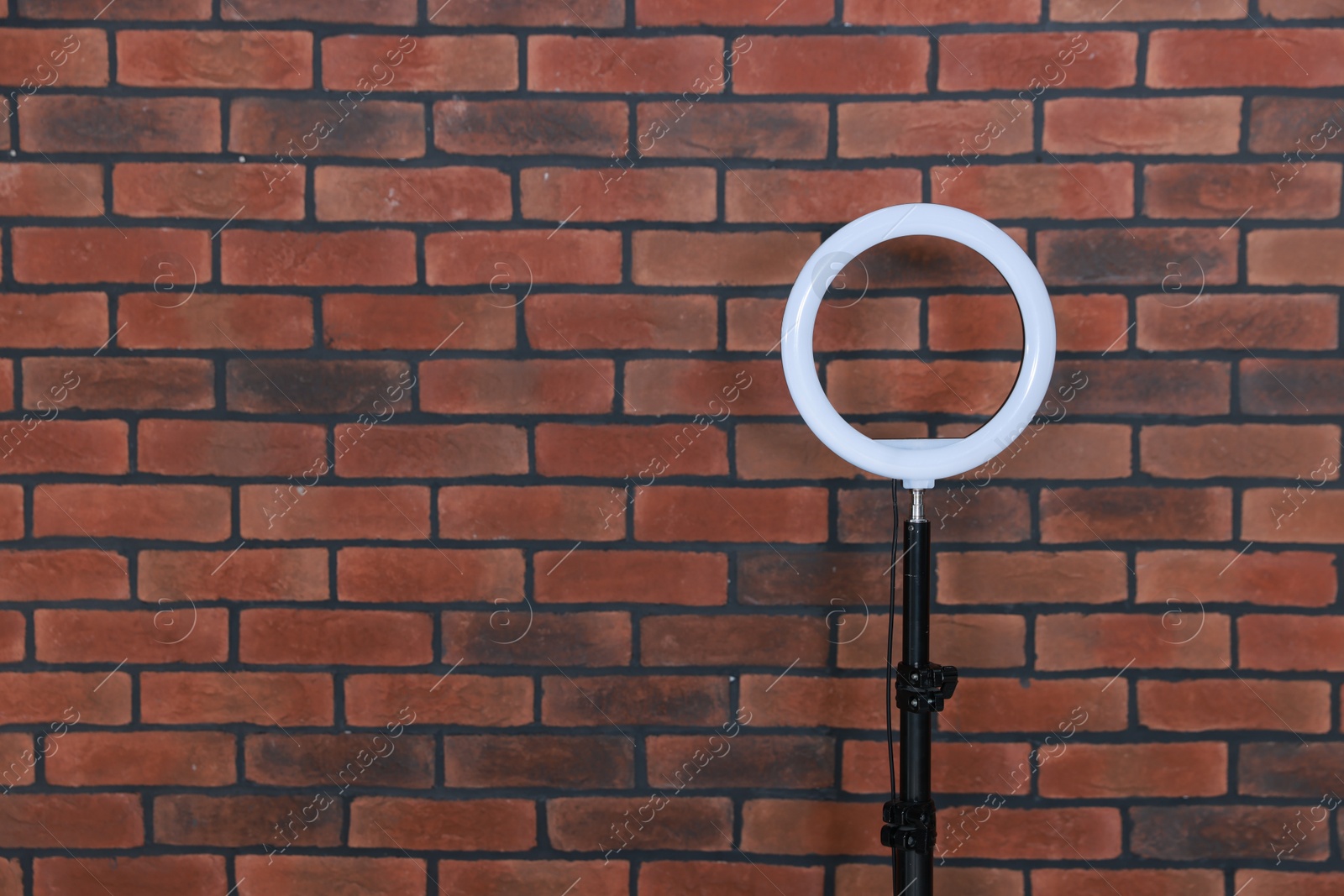 Photo of Ring lamp on stand against brick wall, space for text