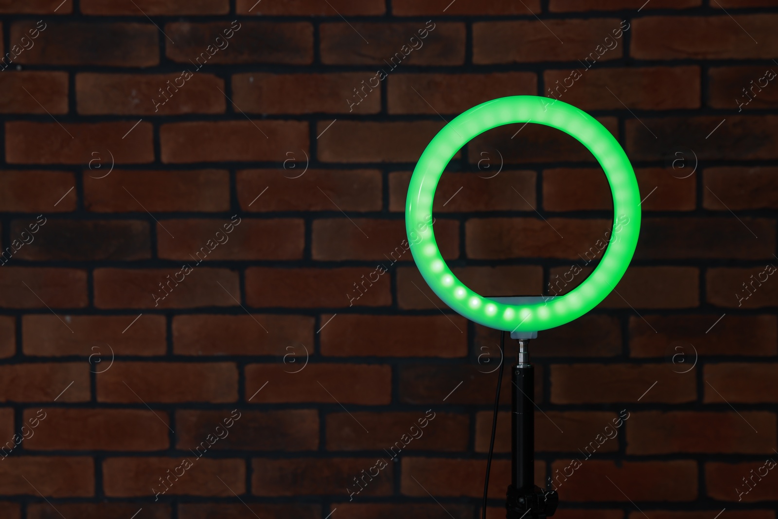 Photo of Ring lamp on stand against brick wall, space for text