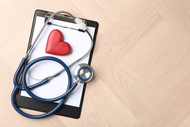 Photo of Cardiology. Clipboard, stethoscope and red decorative heart on wooden table, top view. Space for text