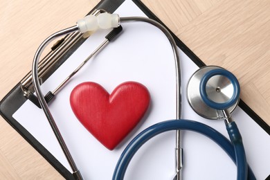 Photo of Cardiology. Clipboard, stethoscope and red decorative heart on wooden table, top view