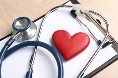 Photo of Cardiology. Clipboard, stethoscope and red decorative heart on wooden table, t closeup