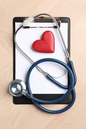 Photo of Cardiology. Clipboard, stethoscope and red decorative heart on wooden table, top view