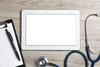 Photo of Cardiology. Tablet, stethoscope, clipboard and pen on wooden table, flat lay