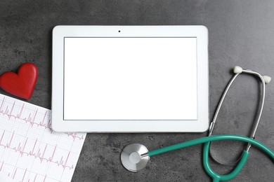 Photo of Cardiology. Tablet, cardiogram, stethoscope and red decorative heart on gray textured table, flat lay