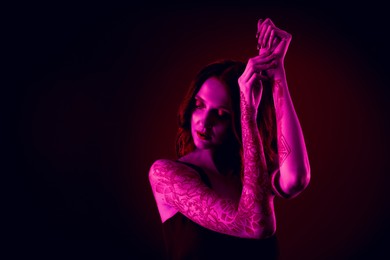 Image of Beautiful woman with tattoos on arms in neon light, space for text