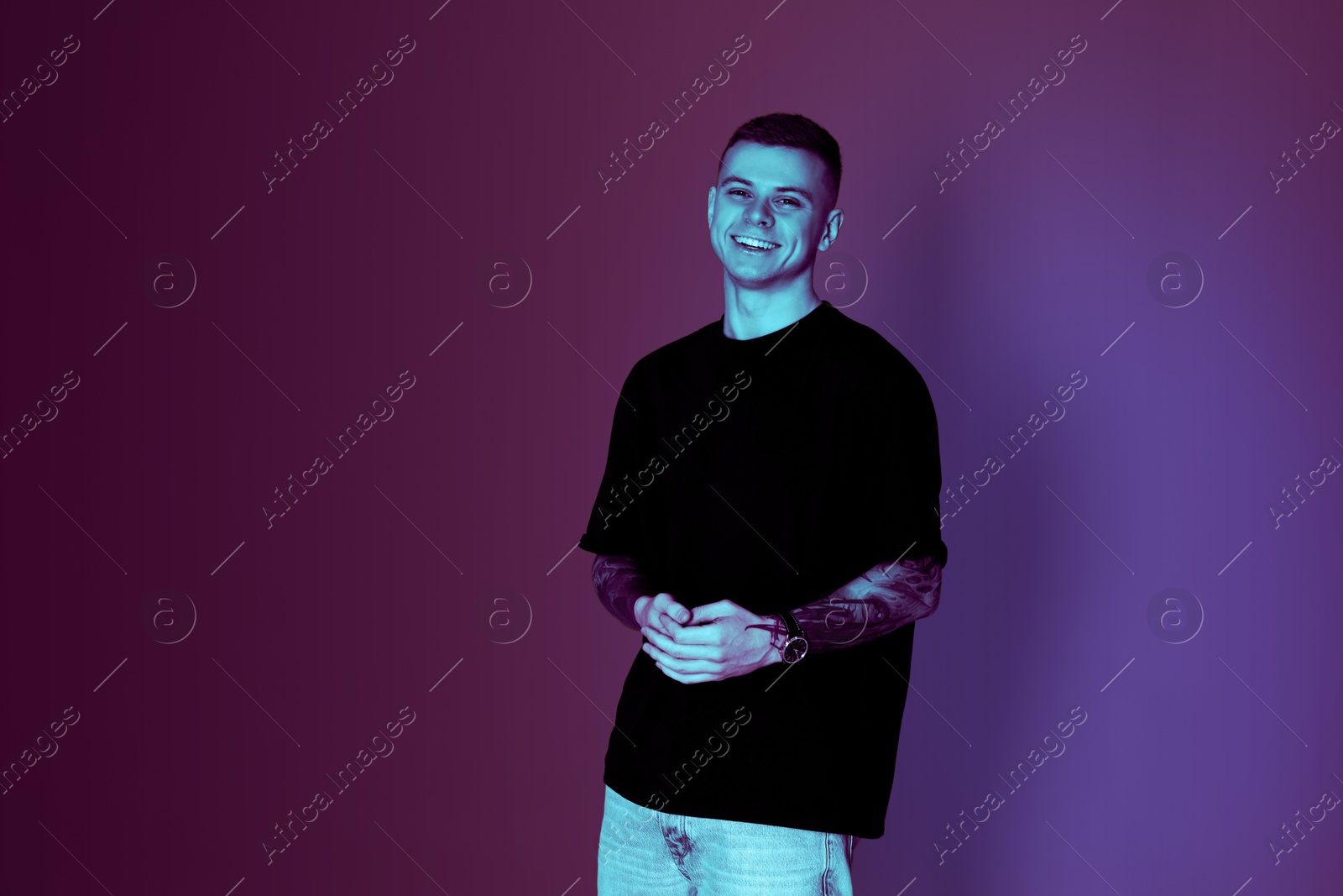 Image of Smiling young man with tattoos in neon light, space for text