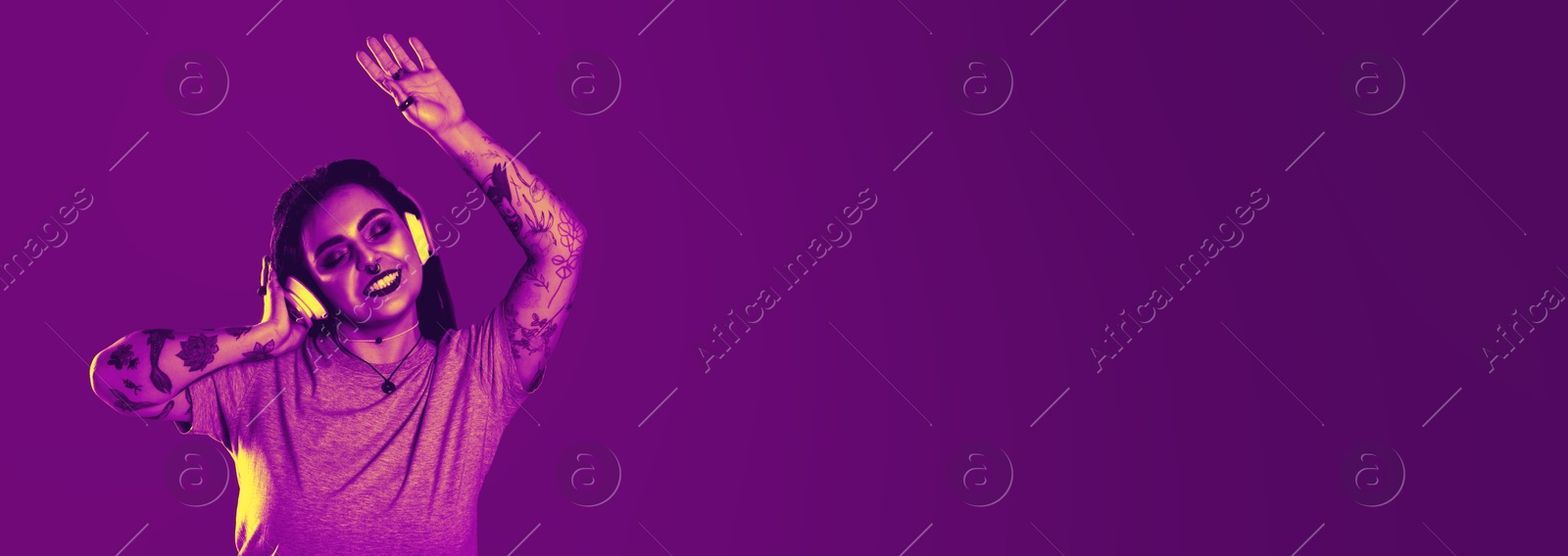 Image of Beautiful young woman with tattoos on arms, nose piercing and dreadlocks listening to music in neon light, space for text. Banner design